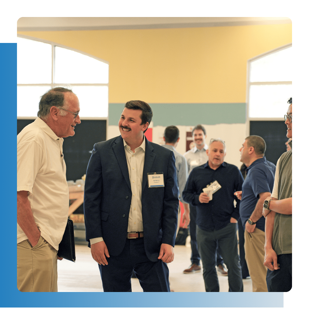 Business professionals networking at a manufacturing industry event, with a Charles IT team member engaged in conversation.