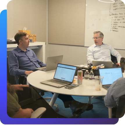 Charles IT team members meeting around a table with laptops during a strategy discussion.
